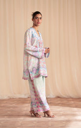 Woman wearing a pastel floral outfit against a beige curtain background