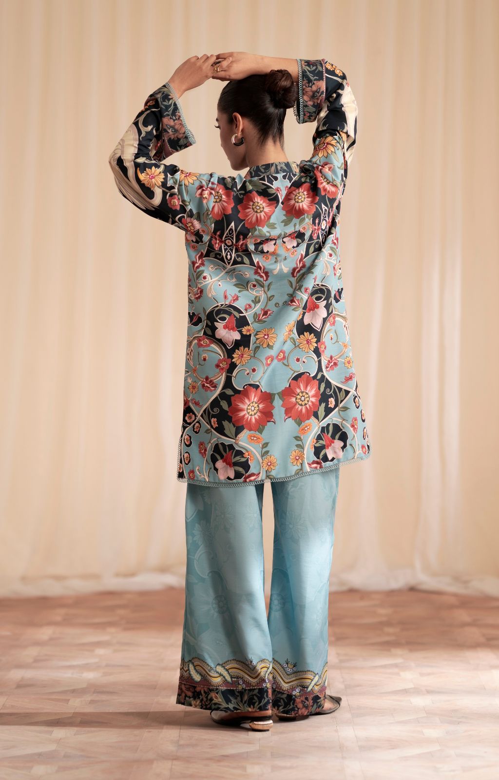 Woman wearing a floral top and light blue pants against a beige curtain background