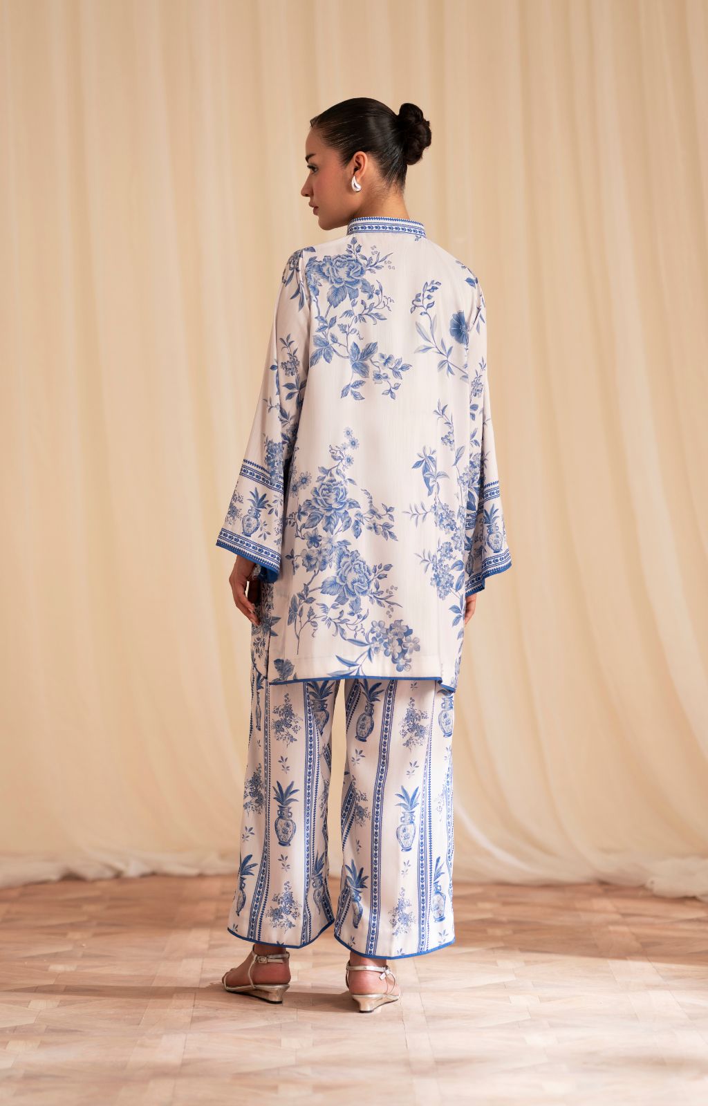 Woman wearing a blue and white floral outfit against a beige curtain background