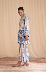 Woman wearing a white outfit with blue patterns against a beige curtain background