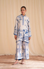 Woman wearing a blue and white floral outfit against a beige curtain background