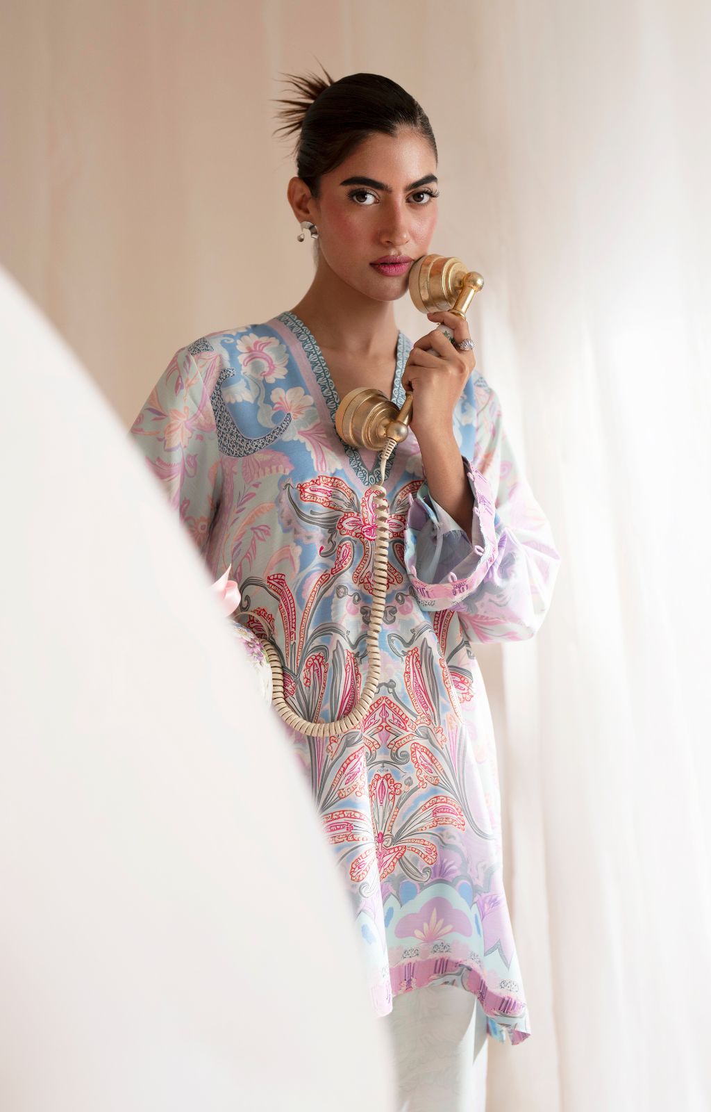 Woman in a patterned dress holding a vintage phone against a plain background