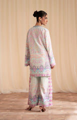 Woman wearing a pastel-colored traditional outfit with a patterned top and pants against a beige curtain background.