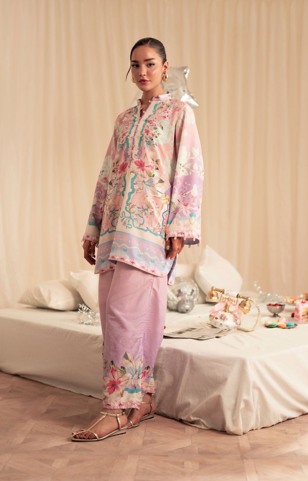 Woman in a floral outfit standing in a room with a bed and decorative items.