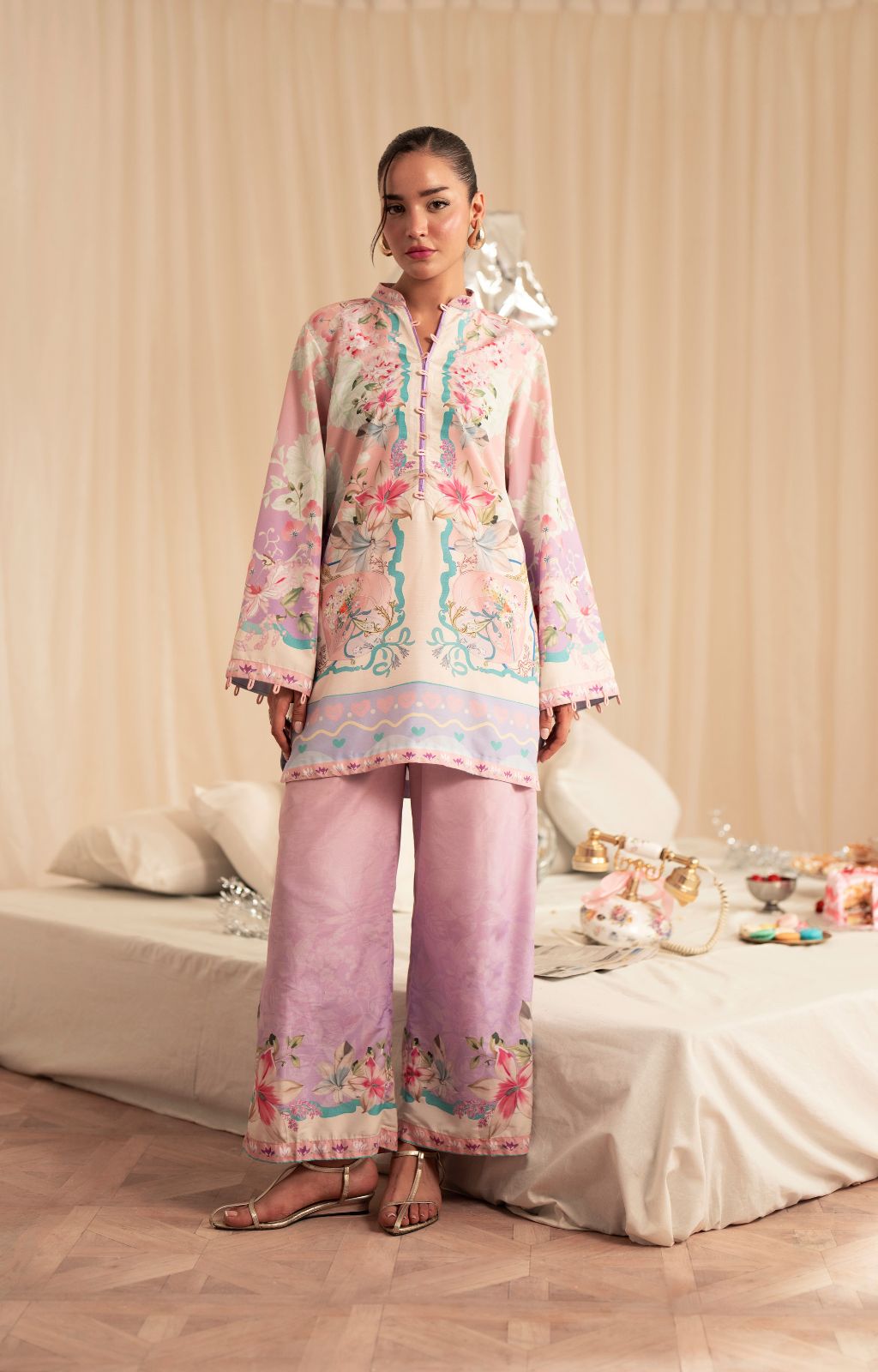 Woman wearing a pastel floral outfit standing in a decorated room with a bed and decorative items.