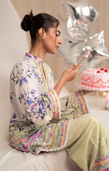 Woman in a colorful outfit holding a cake with balloons in the background