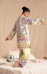 Woman wearing a floral outfit on a bed with decorative items.