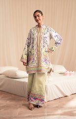 Woman wearing a floral embroidered outfit in a room with a bed and pillows.