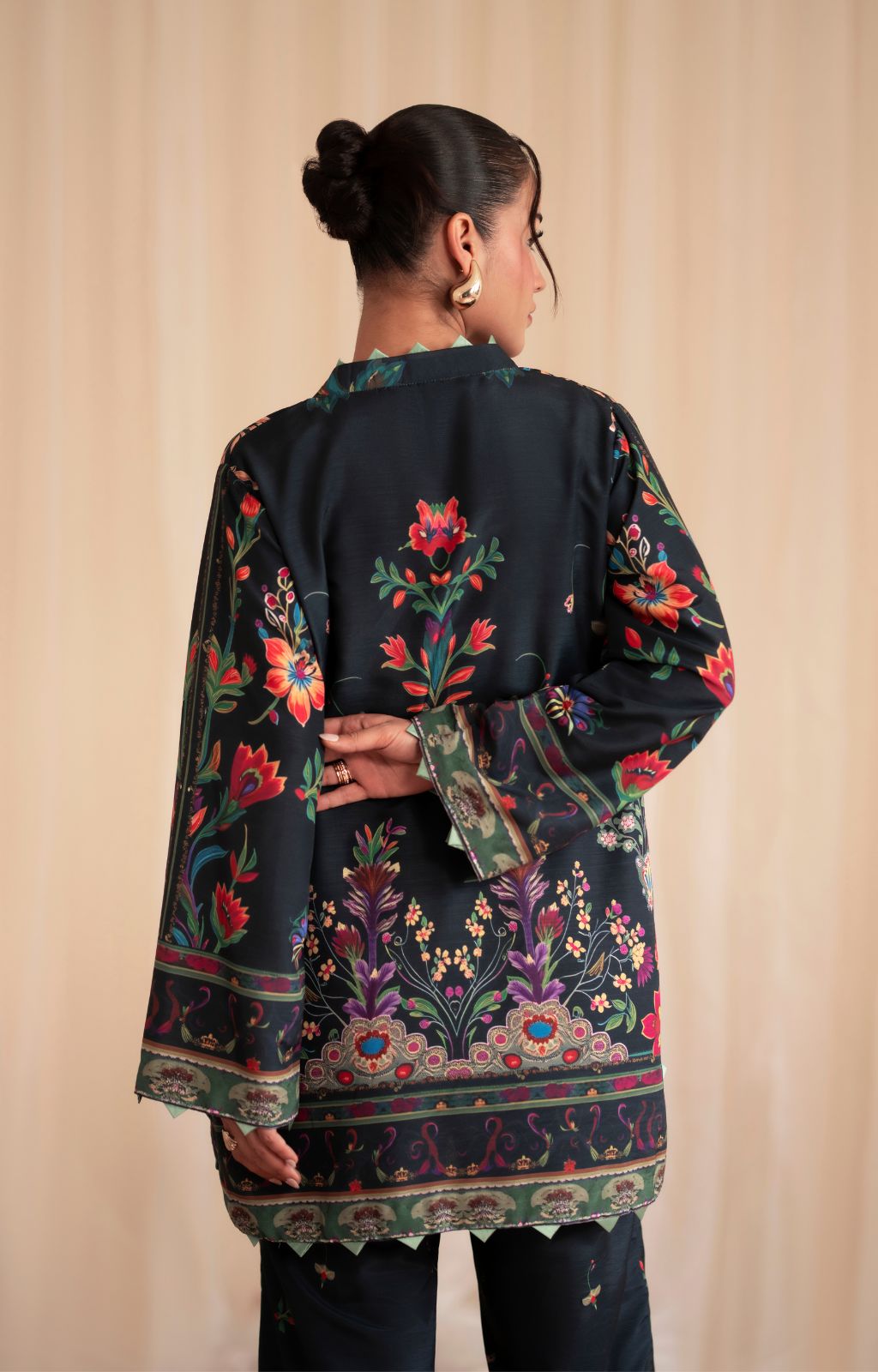 Woman wearing a black embroidered traditional outfit against a beige background
