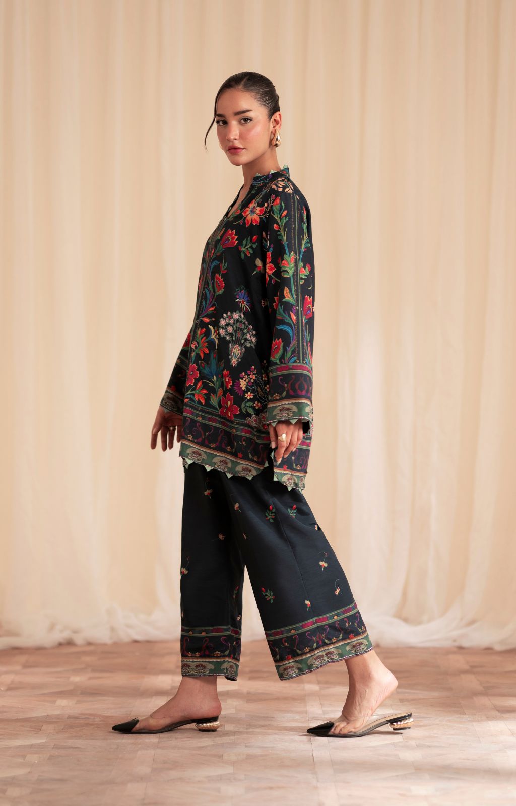 Woman wearing a dark floral top and pants against a beige curtain background