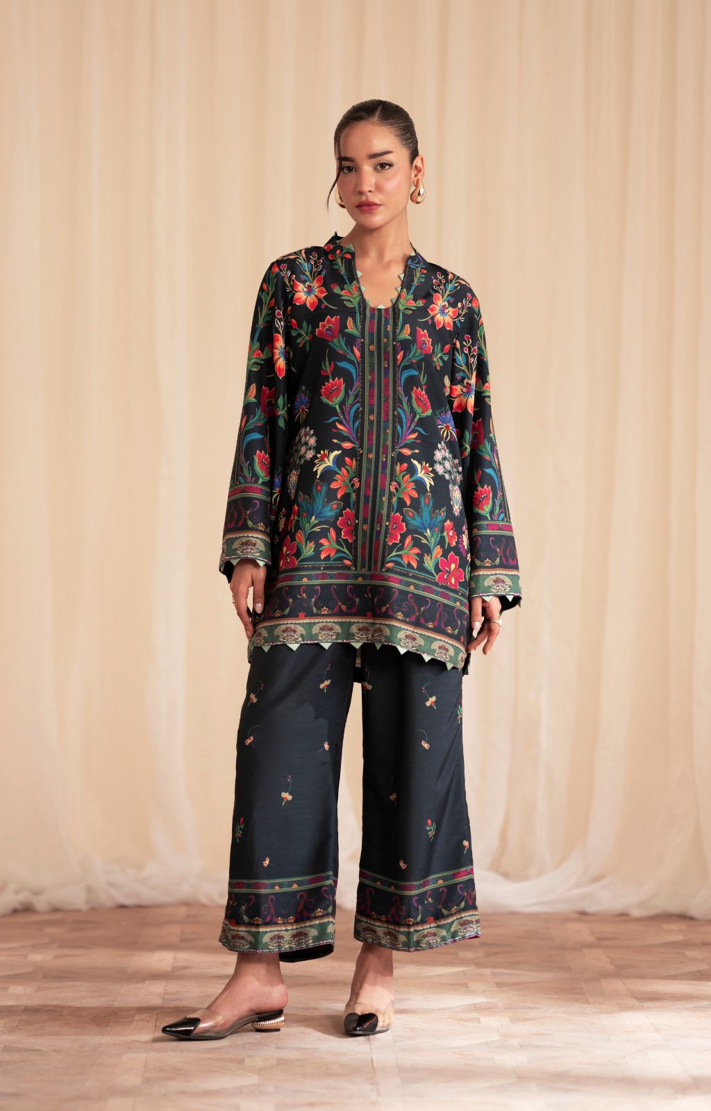 Woman wearing a floral top and dark pants against a beige curtain background