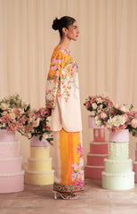 Woman in a floral outfit standing among decorated cakes and flowers.