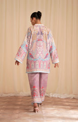 Person wearing a colorful embroidered outfit walking on a wooden floor with a beige curtain background