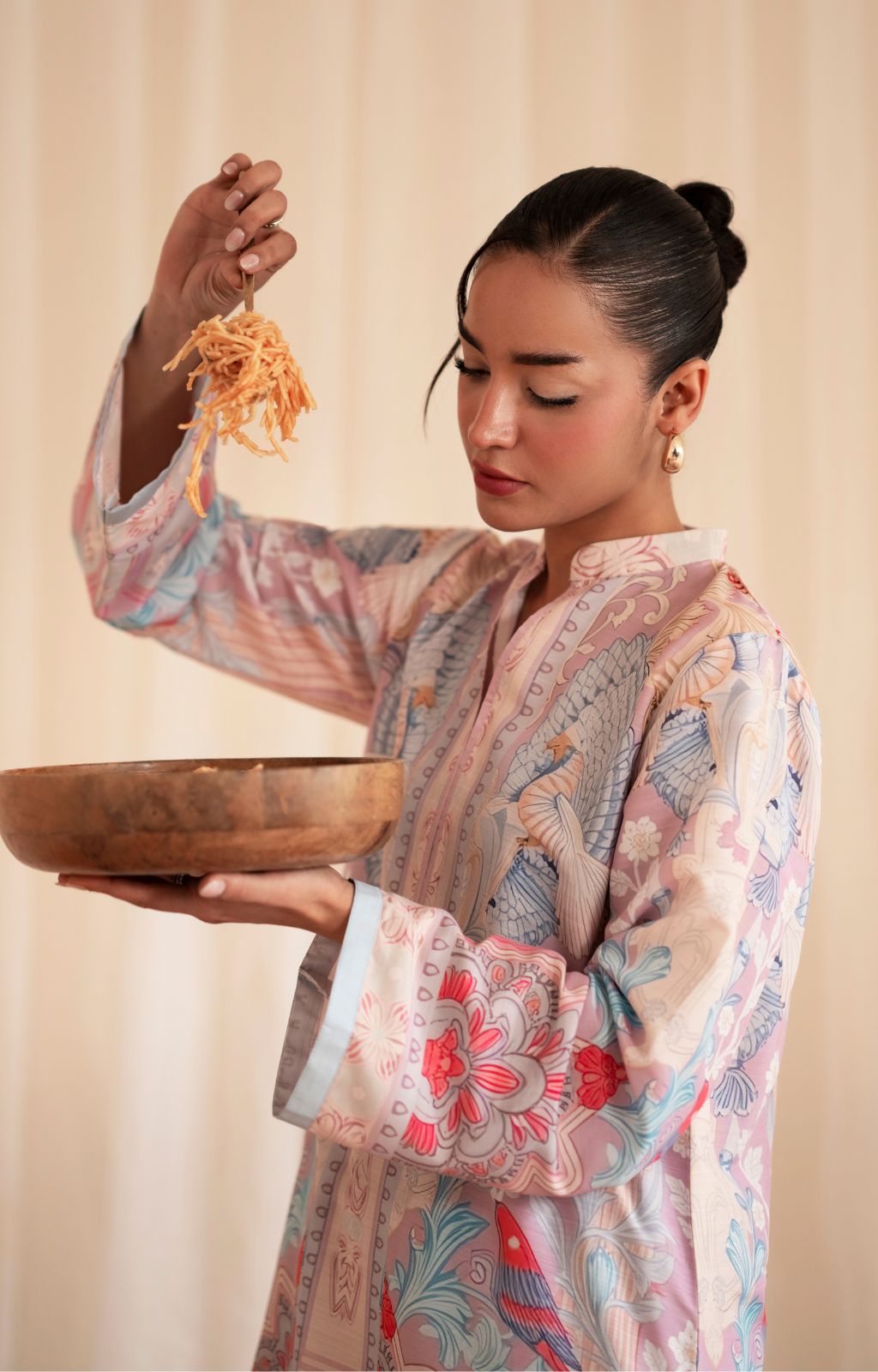 Woman in a floral kimono holding a wooden bowl and noodles against a beige background