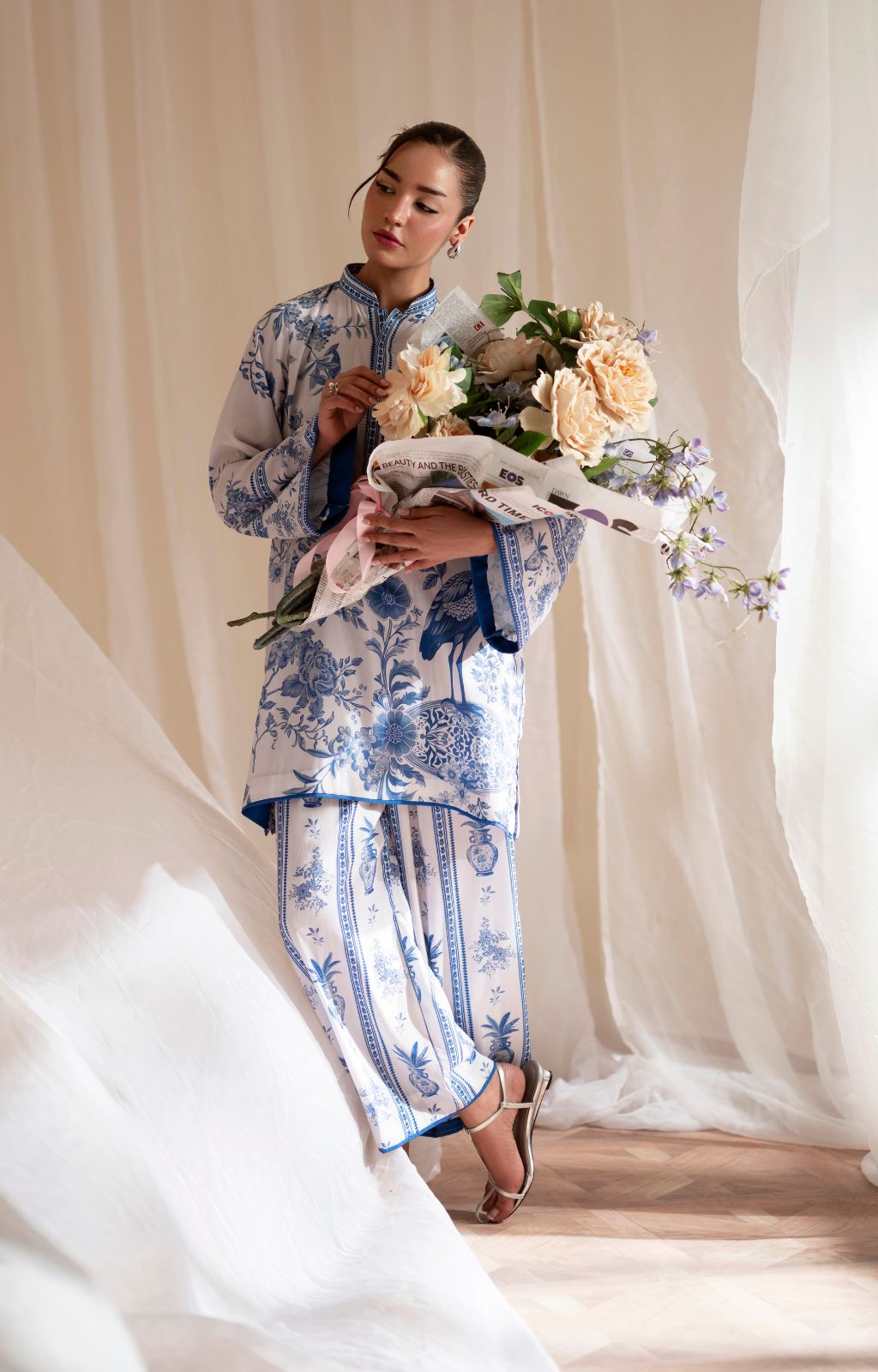 Woman in a traditional outfit holding flowers against a soft, neutral background